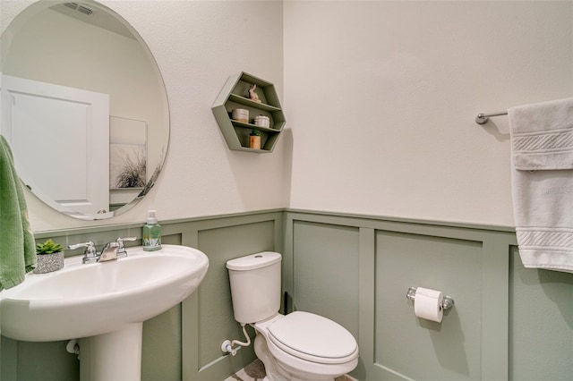 bathroom with a wainscoted wall, a sink, toilet, and a decorative wall