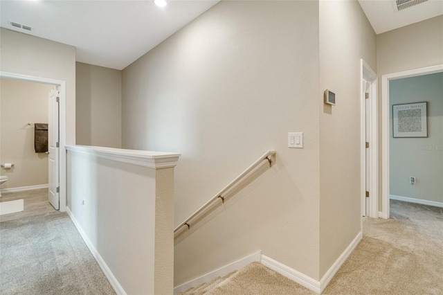 hallway with carpet, visible vents, baseboards, and an upstairs landing