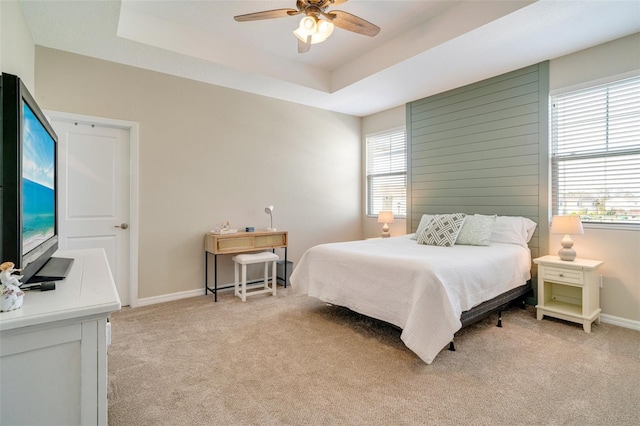 bedroom with light carpet, ceiling fan, a tray ceiling, and baseboards