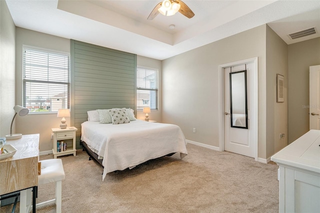 bedroom with light carpet, a ceiling fan, visible vents, baseboards, and a raised ceiling