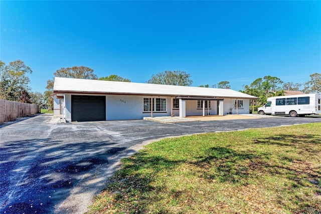 ranch-style house with a front lawn, fence, an attached garage, and aphalt driveway