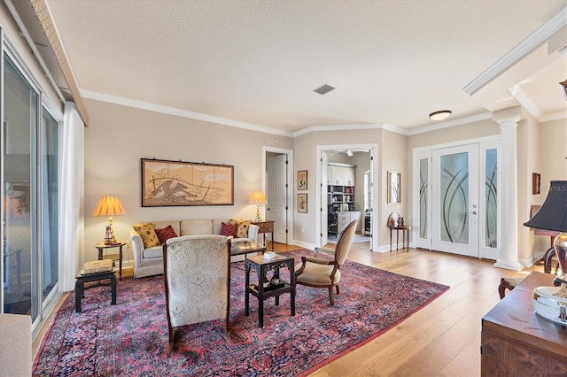 living area with decorative columns, crown molding, visible vents, and hardwood / wood-style floors