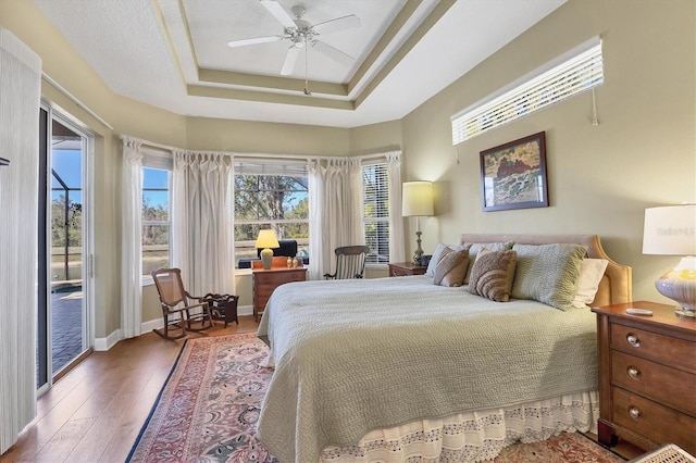 bedroom featuring ceiling fan, wood finished floors, baseboards, access to outside, and a raised ceiling