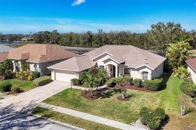 ranch-style house with an attached garage, roof with shingles, decorative driveway, stucco siding, and a front yard