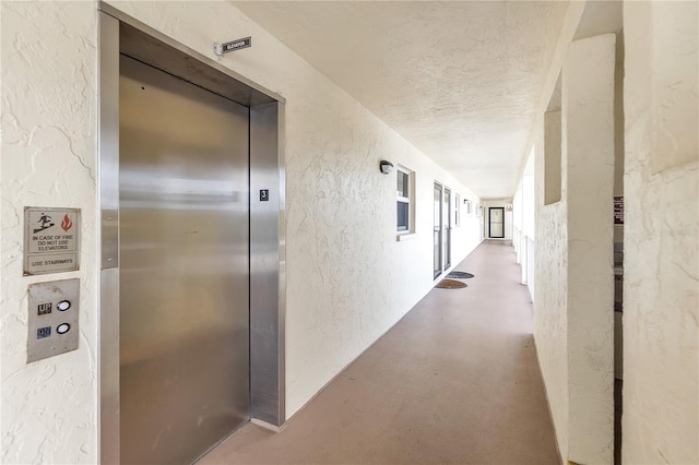 corridor with a textured ceiling, a textured wall, finished concrete flooring, and elevator