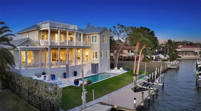 back of house at dusk with a fenced in pool, a balcony, boat lift, a water view, and a patio area