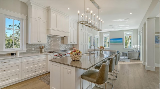 kitchen with a kitchen island with sink, a sink, white cabinetry, a kitchen breakfast bar, and custom range hood