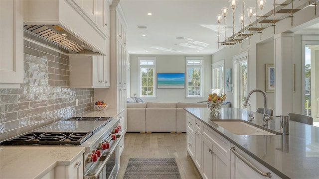 kitchen featuring light stone counters, open floor plan, a sink, high end stove, and premium range hood