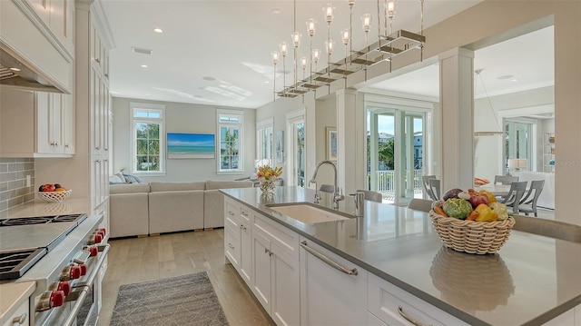 kitchen with a center island with sink, white cabinets, high end stainless steel range, hanging light fixtures, and a sink