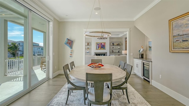 dining space with ornamental molding, a large fireplace, wine cooler, and wood finished floors