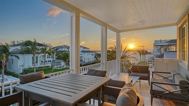 balcony at dusk with a sunroom, a residential view, outdoor dining area, and an outdoor hangout area