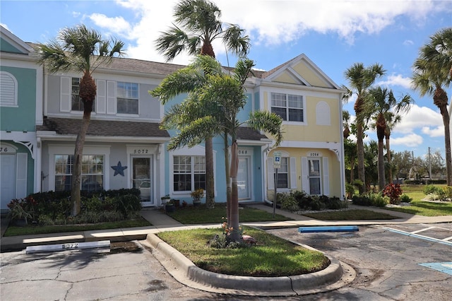 townhome / multi-family property with uncovered parking, a shingled roof, and stucco siding