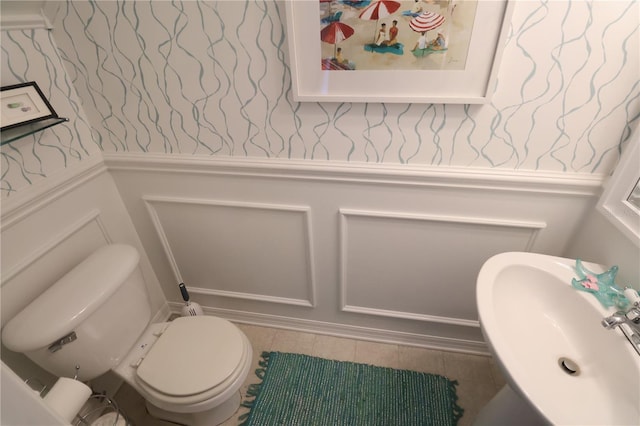 half bathroom featuring a wainscoted wall, a decorative wall, toilet, a sink, and wallpapered walls