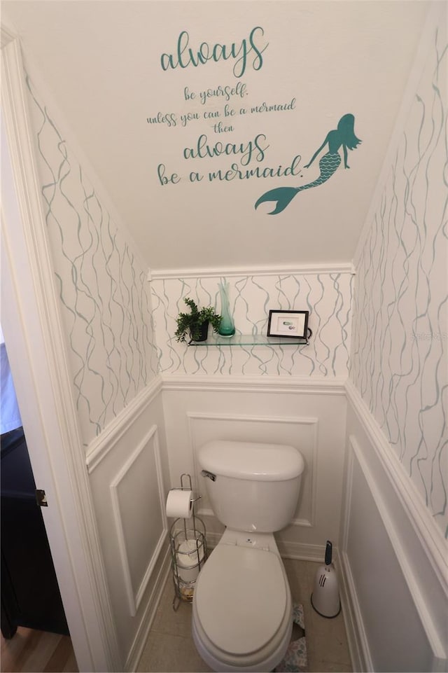 bathroom featuring wainscoting, a decorative wall, toilet, and wallpapered walls