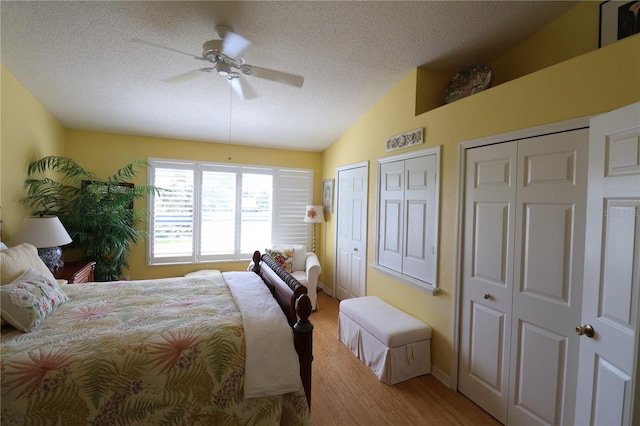 bedroom featuring ceiling fan, a textured ceiling, wood finished floors, multiple closets, and vaulted ceiling