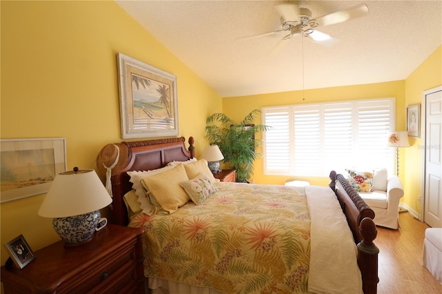 bedroom featuring light wood-type flooring, lofted ceiling, a textured ceiling, and a ceiling fan