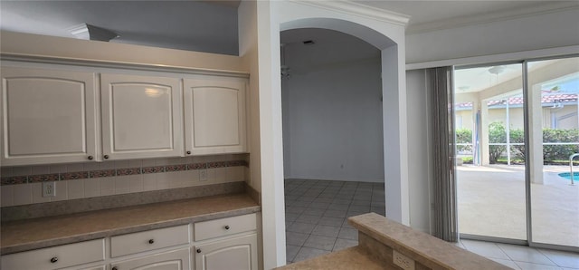 kitchen featuring arched walkways, light tile patterned flooring, white cabinets, ornamental molding, and backsplash