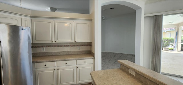 kitchen with light tile patterned floors, tasteful backsplash, arched walkways, white cabinets, and freestanding refrigerator