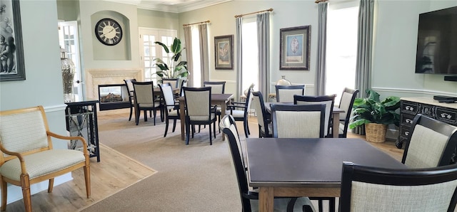 dining room with a high end fireplace, a wealth of natural light, light colored carpet, and crown molding