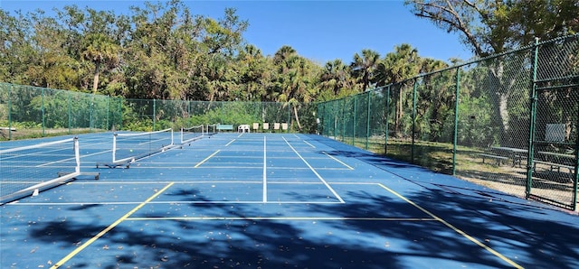 view of sport court featuring fence and a wooded view