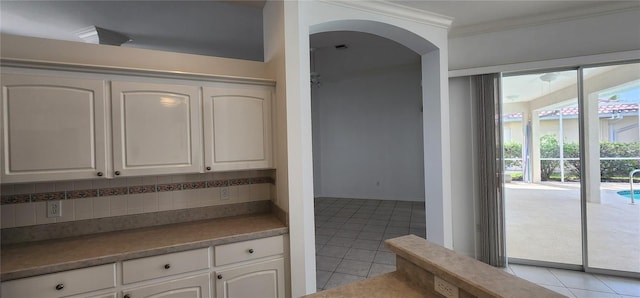 kitchen with light tile patterned floors, tasteful backsplash, arched walkways, ornamental molding, and white cabinets