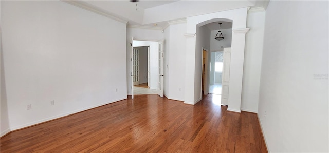 spare room with arched walkways, ornamental molding, wood finished floors, and baseboards