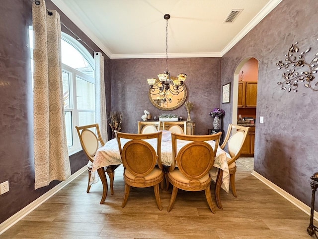 dining area featuring arched walkways, visible vents, baseboards, ornamental molding, and light wood-type flooring