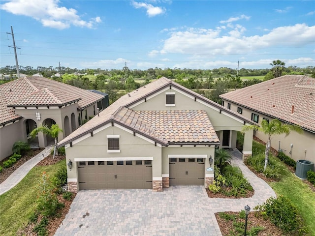 mediterranean / spanish-style home with a garage, stone siding, a tiled roof, decorative driveway, and stucco siding