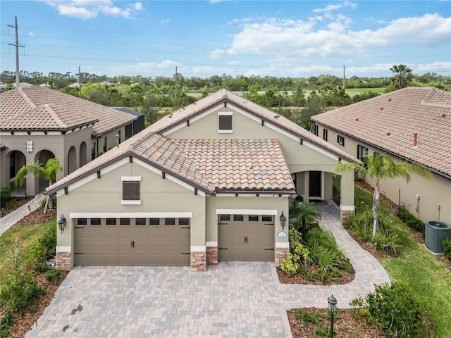 mediterranean / spanish-style house featuring central AC unit, a tiled roof, an attached garage, decorative driveway, and stucco siding