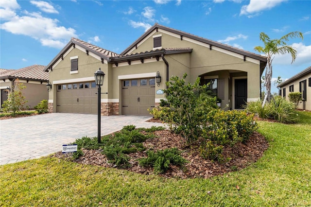 mediterranean / spanish home with decorative driveway, stucco siding, an attached garage, a front yard, and stone siding