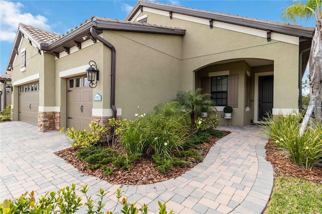 view of front facade featuring stone siding, a tiled roof, an attached garage, decorative driveway, and stucco siding