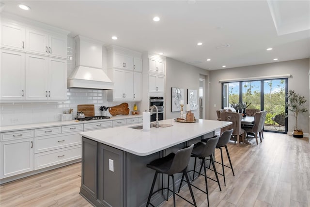 kitchen with gas cooktop, premium range hood, a sink, white cabinets, and decorative backsplash