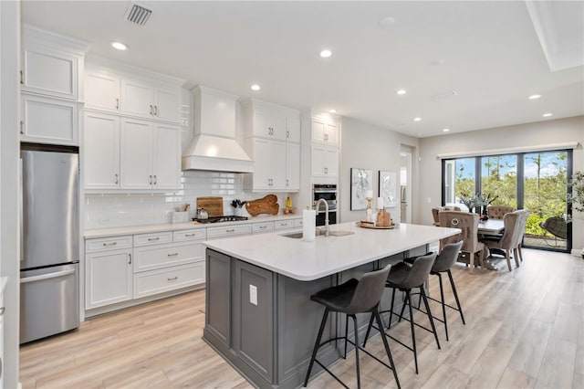 kitchen featuring a sink, white cabinetry, backsplash, freestanding refrigerator, and custom range hood