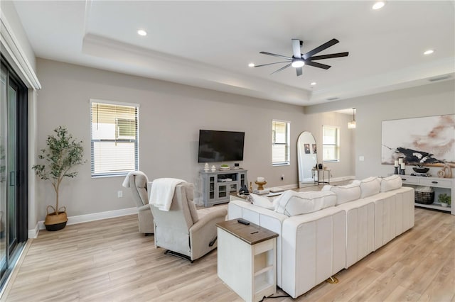 living room featuring baseboards, a tray ceiling, recessed lighting, and light wood-style floors