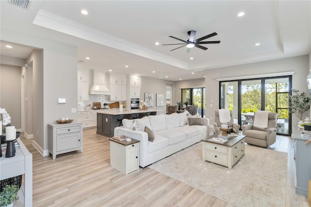 living room with light wood finished floors, a raised ceiling, visible vents, and recessed lighting