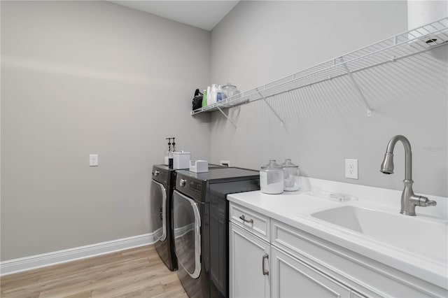 laundry area with cabinet space, baseboards, light wood-style flooring, washing machine and clothes dryer, and a sink