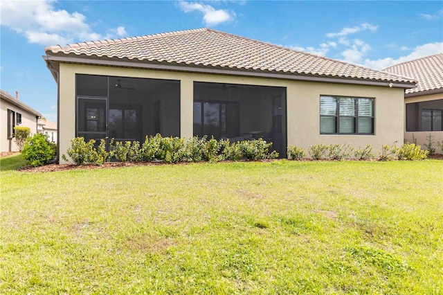 rear view of property with a tiled roof, a lawn, a sunroom, and stucco siding