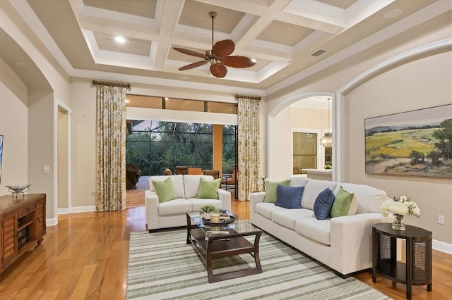 living room featuring arched walkways, a towering ceiling, visible vents, ornamental molding, and light wood-type flooring