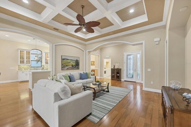 living area featuring light wood-type flooring, coffered ceiling, visible vents, and baseboards