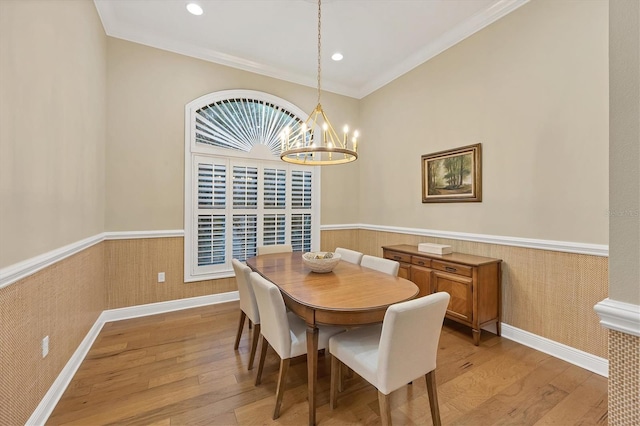 dining area with ornamental molding, a wainscoted wall, light wood finished floors, and an inviting chandelier