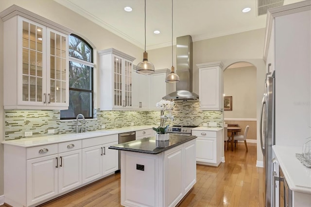 kitchen featuring appliances with stainless steel finishes, arched walkways, white cabinetry, and wall chimney exhaust hood