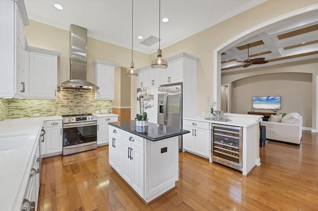 kitchen featuring light wood finished floors, coffered ceiling, wall chimney exhaust hood, wine cooler, and appliances with stainless steel finishes