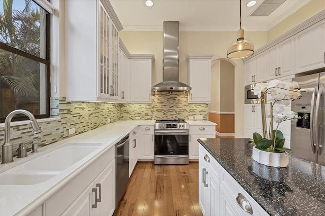 kitchen with a sink, appliances with stainless steel finishes, wall chimney exhaust hood, decorative light fixtures, and crown molding