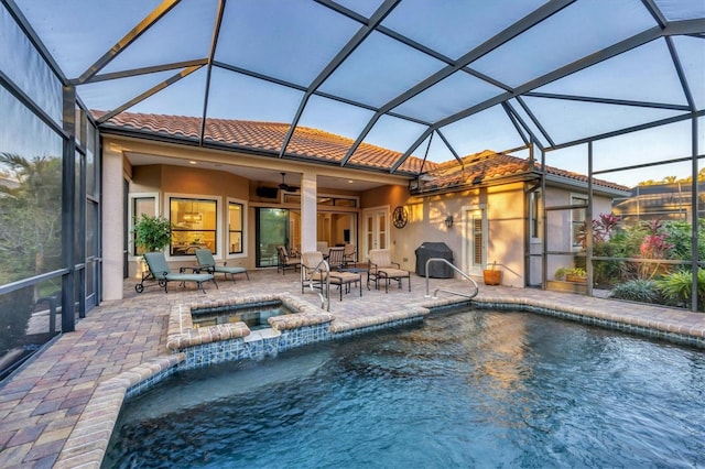 view of swimming pool with glass enclosure, ceiling fan, a grill, a patio area, and a pool with connected hot tub