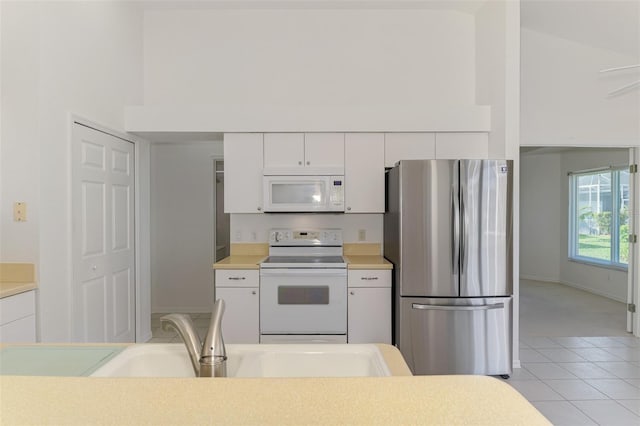 kitchen with a sink, white cabinetry, white appliances, light countertops, and a towering ceiling