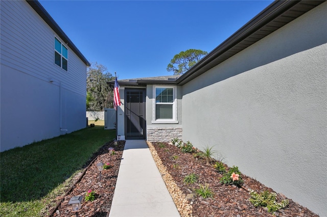 property entrance with stone siding, a lawn, and stucco siding