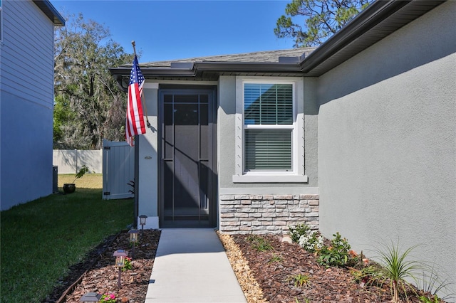 entrance to property featuring stone siding, fence, a lawn, and stucco siding