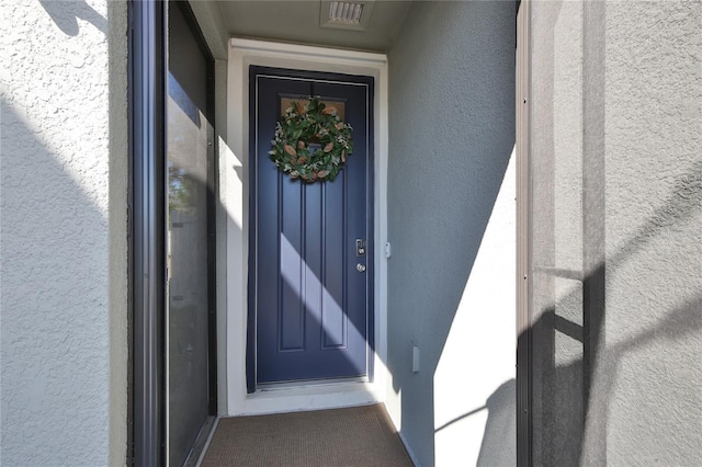 view of exterior entry featuring visible vents and stucco siding