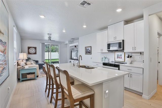 kitchen featuring a center island with sink, electric range oven, a breakfast bar, open floor plan, and a sink