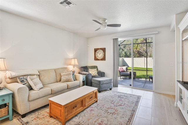 living area with visible vents, a ceiling fan, light tile patterned flooring, a textured ceiling, and baseboards